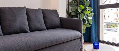 Un sofá gris con cojines, una lámpara de pie, una planta en maceta y una mesita redonda con una vela azul.