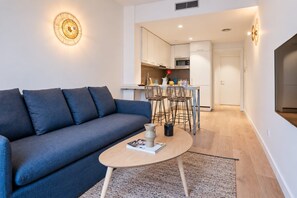 A modern living room with a sofa, a coffee table, and a kitchen in the background. - Sweett | Girona 303 - One Bedroom Apartment, Sleeps 4 (Barcelona)