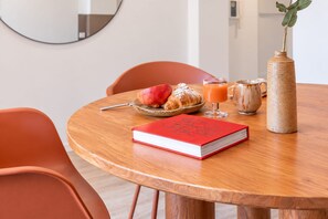A round wooden table with a book, a croissant, a glass of orange juice, a mug, and a woven vase with a plant. - Sweett | Girona 402 - One Bedroom Apartment, Sleeps 4 (Barcelona)