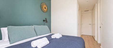 Une chambre à coucher avec un lit, des oreillers, une lampe fixée au mur et une porte donnant sur une autre pièce.