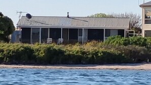 Rannalla sijaitseva talo, jossa on suuri ikkunalla varustettu julkisivu, satelliittiantenni ja pieni kuisti.