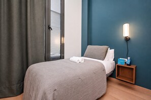 Een hotelkamer met een bed, nachtkastje, wandlamp en een raam met gordijnen.