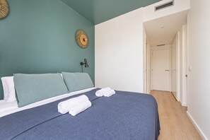 A bedroom with a bed, pillows, a wall-mounted lamp, and a door leading to another room. - Sweett | Girona 502 - One Bedroom Apartment, Sleeps 4 (Barcelona)