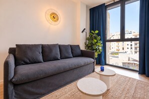 A modern living room with a sofa, a small round table, a floor lamp, and a large window with curtains. - Sweett | Girona 502 - One Bedroom Apartment, Sleeps 4 (Barcelona)