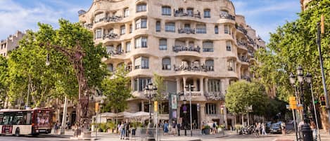 A multi-story building with balconies, a street in front, and trees.