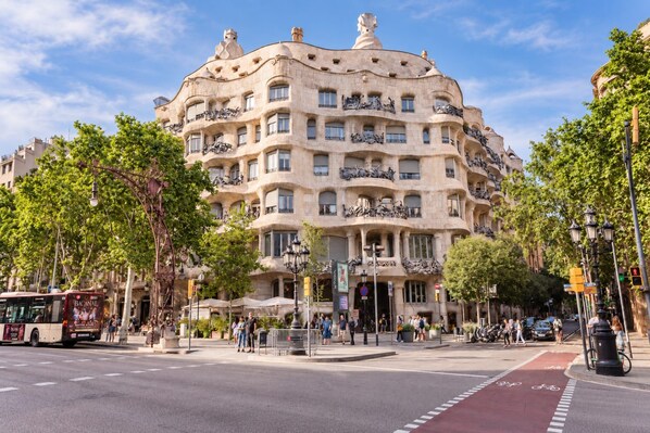 A multi-story building with balconies, a street in front, and trees.