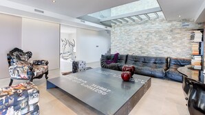 A modern living room with a stone wall, a sofa, a coffee table with writing, and a chair with a collage design. - Villa "Atalaya" with Sea View, Private Pool & Wi-Fi (Peñíscola)