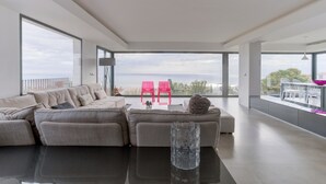 A modern living room with a large sectional sofa, a glass coffee table, and a view of the sea through large windows. - Villa "Atalaya" with Sea View, Private Pool & Wi-Fi (Peñíscola)
