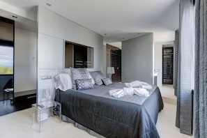 A modern bedroom with a large bed, a bedside table, a mirror, and a view of the outside.