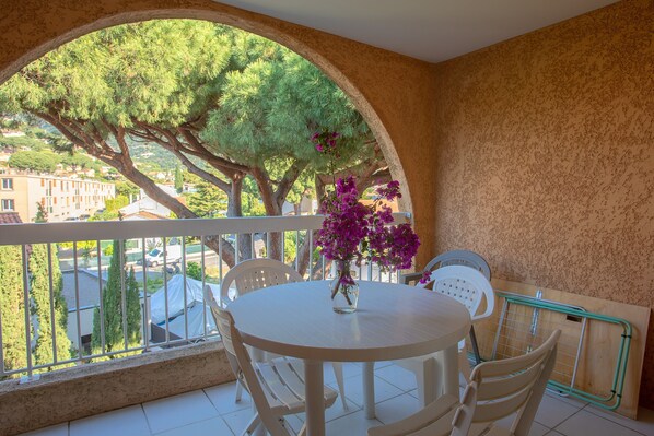 A balcony with a round table and chairs, a vase with flowers, and a view of trees and buildings.