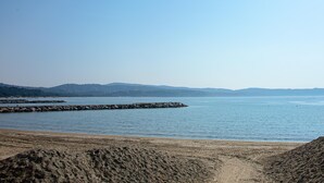 Ranta, jossa on kivinen aallonmurtaja, tyyni vesi ja kaukana kohoavat kukkulat.
