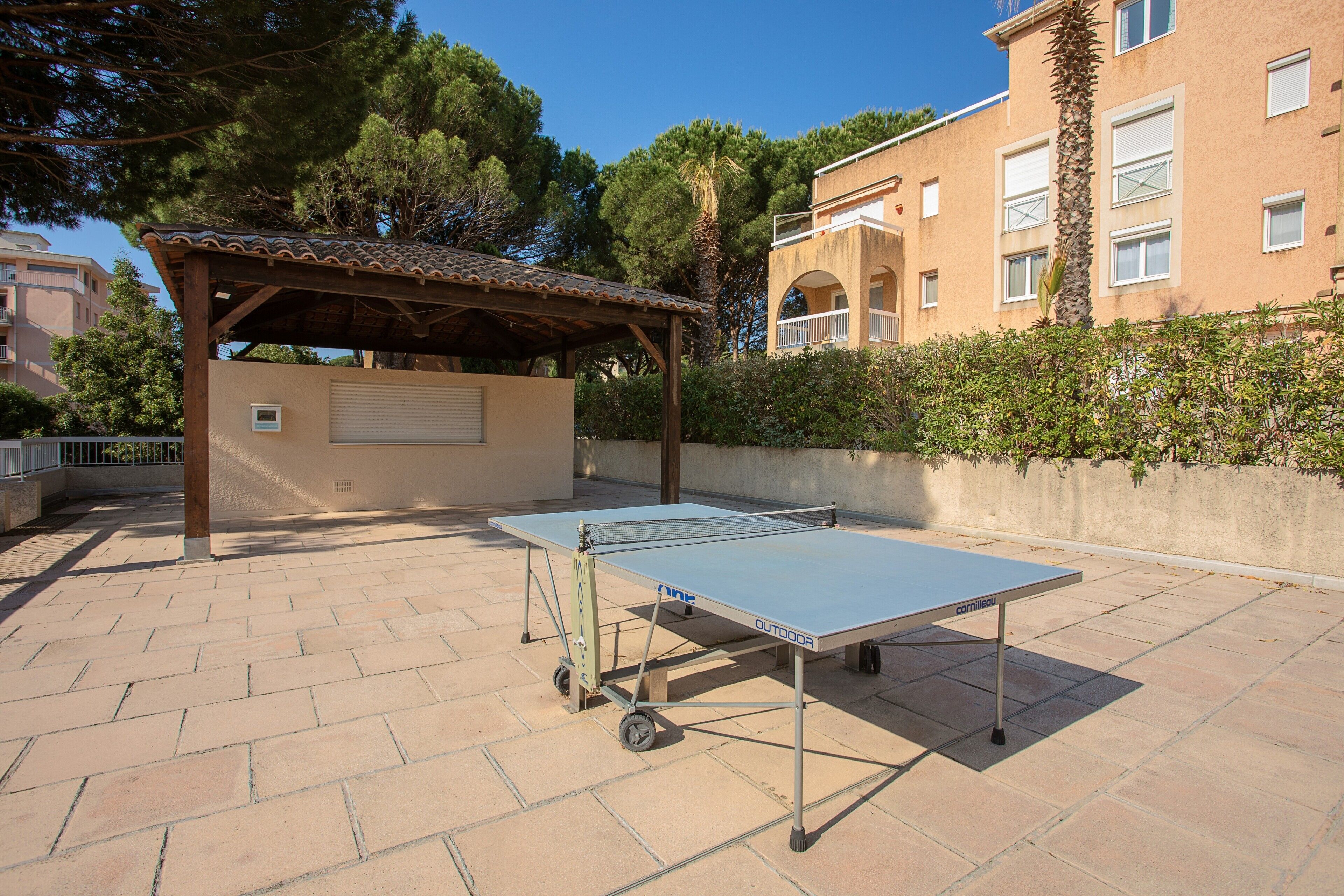 Un tavolo da ping pong all'aperto su un patio lastricato, con una pergola sullo sfondo.
