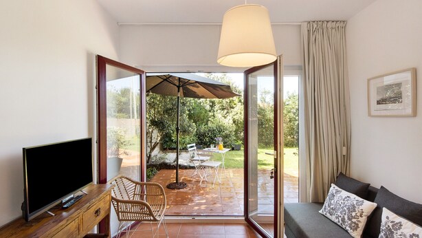 A living room with a TV, sofa, and a dining area with an umbrella.