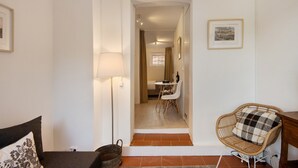 A hallway leading to a dining area with a table and chairs, a wicker chair with a checkered cushion, and a lamp.