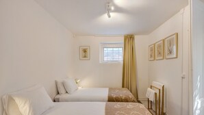 A hotel room with two beds, a window with curtains, framed artwork on the wall, and a towel rack.