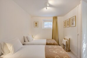 Une chambre d’hôtel avec deux lits, une fenêtre avec des rideaux, des œuvres d’art encadrées au mur et un porte-serviettes.