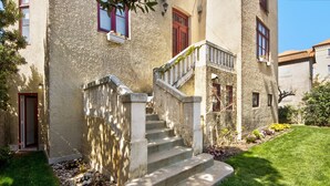 A building with a stone staircase leading to a door, surrounded by a well-maintained lawn and small plants.