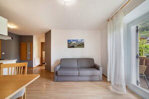A modern living room with a grey sofa, wooden dining table, and a large window with curtains.