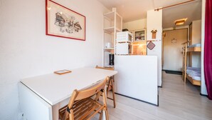 Ett kompakt kök med ett vitt bord och stolar, ett kylskåp och en mikrovågsugn.