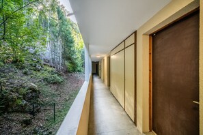 A corridor with a concrete floor, wooden doors, and a view of a forested area.
