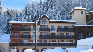 Ett hotell med flera våningar och balkonger, en parkeringsplats med snöbelagda bilar och en snötäckt skog i bakgrunden.