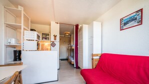 Ett kompakt vardagsrum med ett litet kök, en röd soffa och ett inramat foto på väggen.