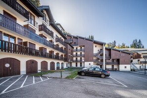 Um hotel com vários andares, varandas, área de estacionamento e um carro estacionado em frente.