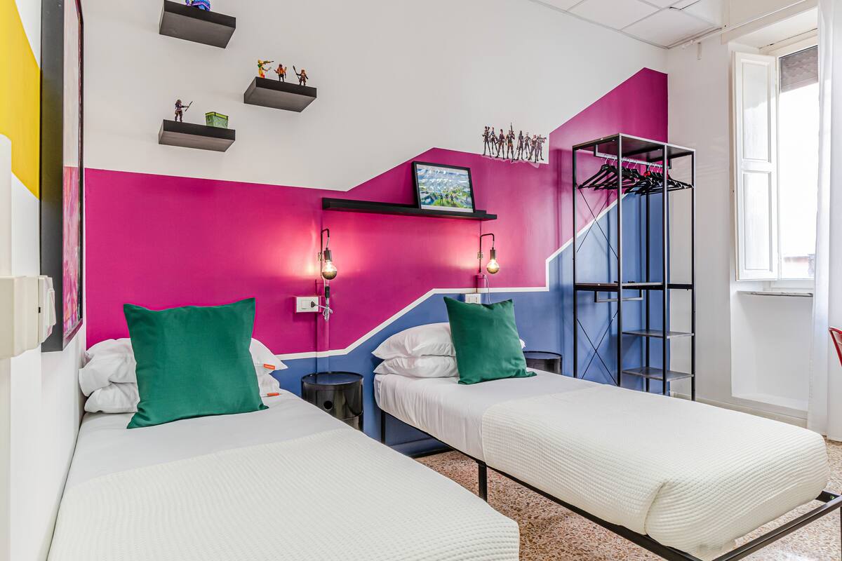 Una habitación de hotel moderna con dos camas, una pared de acento rosa vibrante y un perchero.