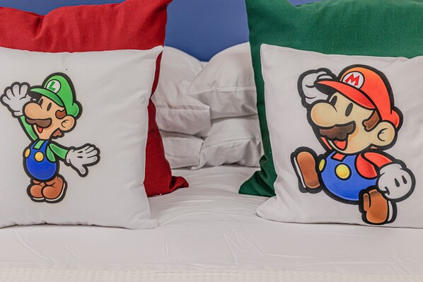 Two pillows with Mario and Luigi characters, a white bedspread, and a red and green pillow.