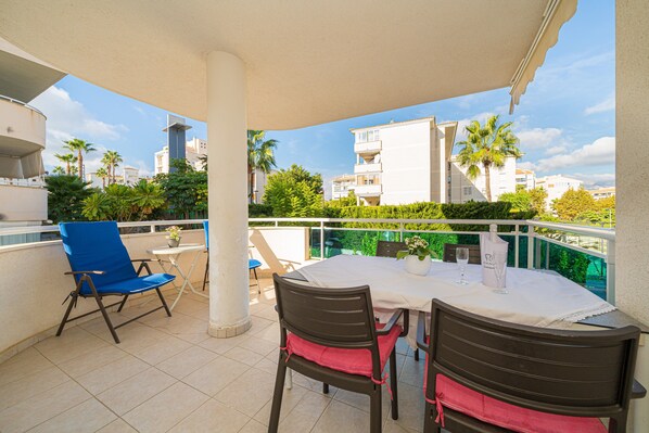 A balcony with a table and chairs, a potted plant, and a view of buildings and palm trees.