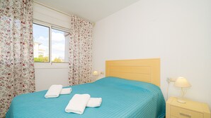 Un dormitorio con cama, cortinas, mesita de noche y lámpara.