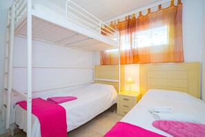 A bunk bed room with a window, a bedside table with a lamp, and a nightstand.