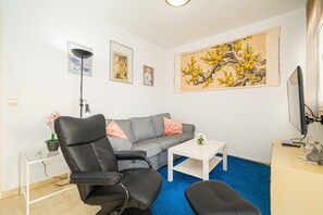A modern living room with a grey sofa, black leather chairs, a white coffee table, and a large painting of a tree.