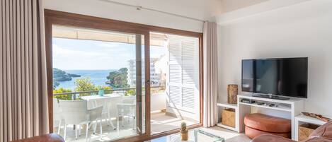 Un salon moderne doté d’un grand téléviseur, d’un canapé en cuir, d’une table basse en verre et d’un balcon offrant une vue sur la mer.