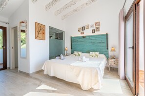 A bedroom with a large bed, a wooden headboard, a mirror, a small table with a lamp, and a door leading to a balcony.