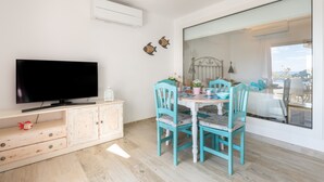 Ein modernes Wohnzimmer mit Flachbildfernseher, einem Esstisch mit Stühlen und einem großen Fenster.