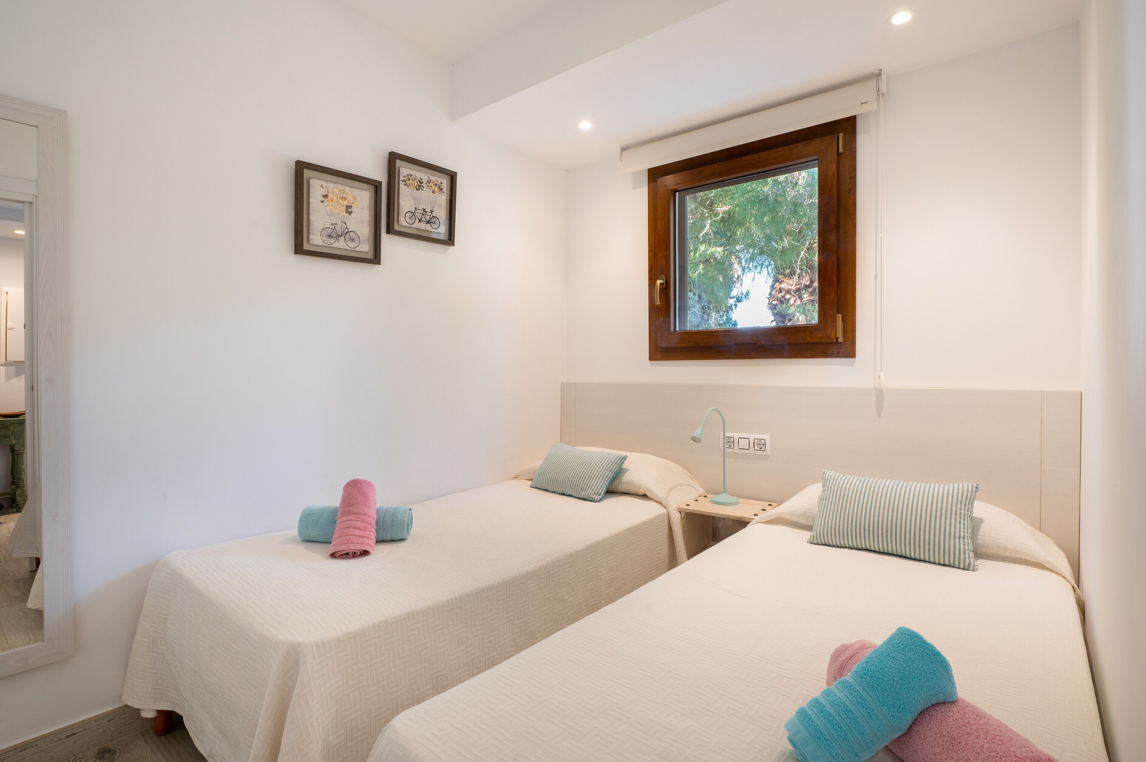 Habitación de hotel con dos camas, una ventana y dos cuadros en la pared.