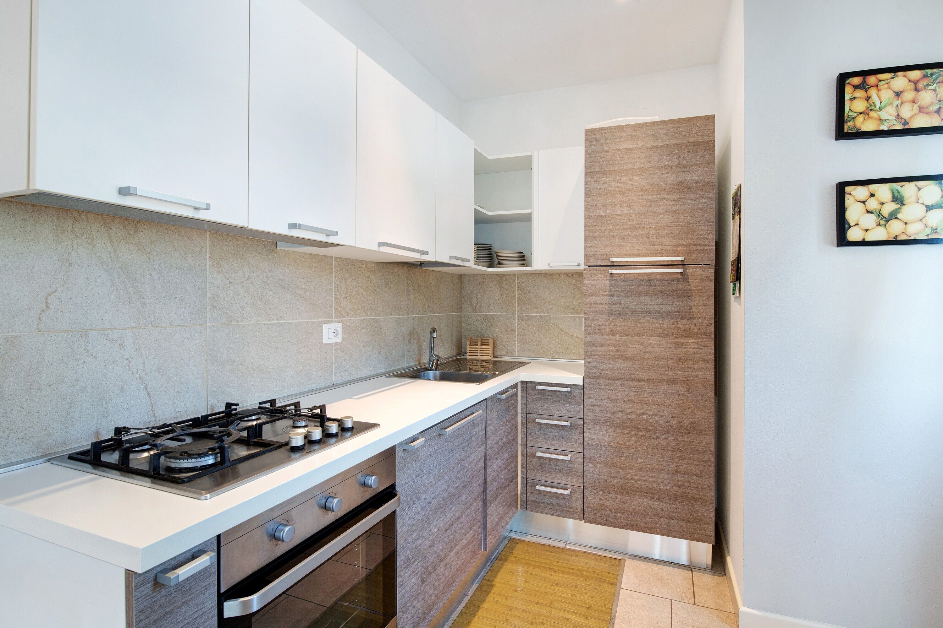 Une cuisine moderne équipée d’une cuisinière à gaz, d’un four et d’un évier. On y trouve des armoires blanches, un mur recouvert de panneaux en bois et un pare-feu en carrelage.
