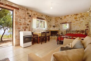 A room with stone walls, a dining table, chairs, a sofa, a small stove, and a fireplace.