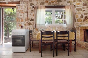 A stone-walled room with a kitchen area, a dining table with chairs, and a window with curtains.