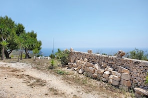 Un mur de pierres, un paysage accidenté, des arbres et une vue dégagée sur la mer.
