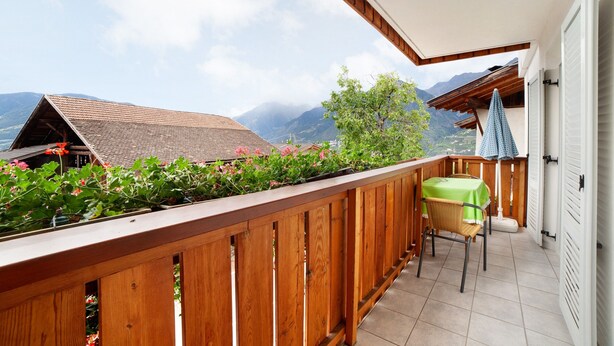 Een balkon met houten leuning, een tafel met een groene tafelkleed en een stoel.