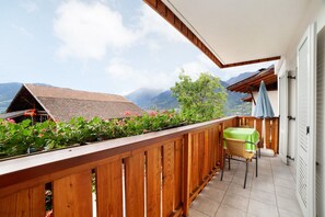 Un balcon avec une balustrade en bois, une table recouverte d’une nappe verte et une chaise.