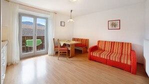 Een kamer met een bank, een eettafel met stoelen, een raam met gordijnen en een plafondlamp.