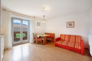 Une pièce comprenant un canapé, une table à manger avec des chaises, une fenêtre avec des rideaux et un luminaire au plafond.