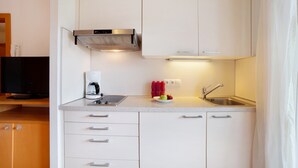 Een compacte keuken met witte kastjes, een roestvrijstalen afzuigkap, een koffiezetapparaat, een spoelbak en een klein schaaltje fruit.