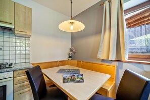 Un rincón comedor con una mesa, sillas, una revista y una ventana con cortinas.