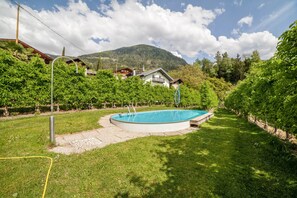 Una piscina rodeada de un césped cuidado, con una casa y montañas al fondo.