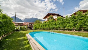 A swimming pool with a wooden deck, surrounded by lush greenery and a mountainous backdrop.
