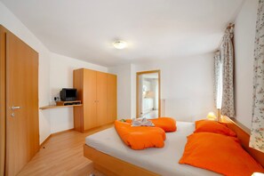 Ein Schlafzimmer mit einem Bett, einem Fernseher auf einem Regal, einem Spiegel und einem Fenster mit Vorhängen.